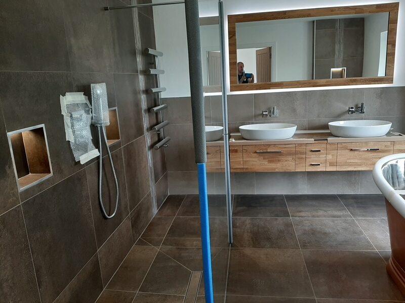 Walk-in shower tiled in large dark porcelain, with a recessed shelf cut into the tiling and a mirror reflecting twin basins