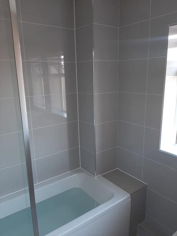The same pale grey bathroom seen from the doorway, with the bath and glass screen against a window