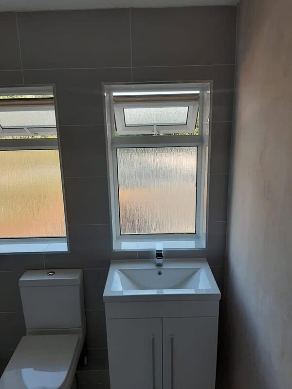 White vanity unit and toilet below two windows, tiled in matt grey