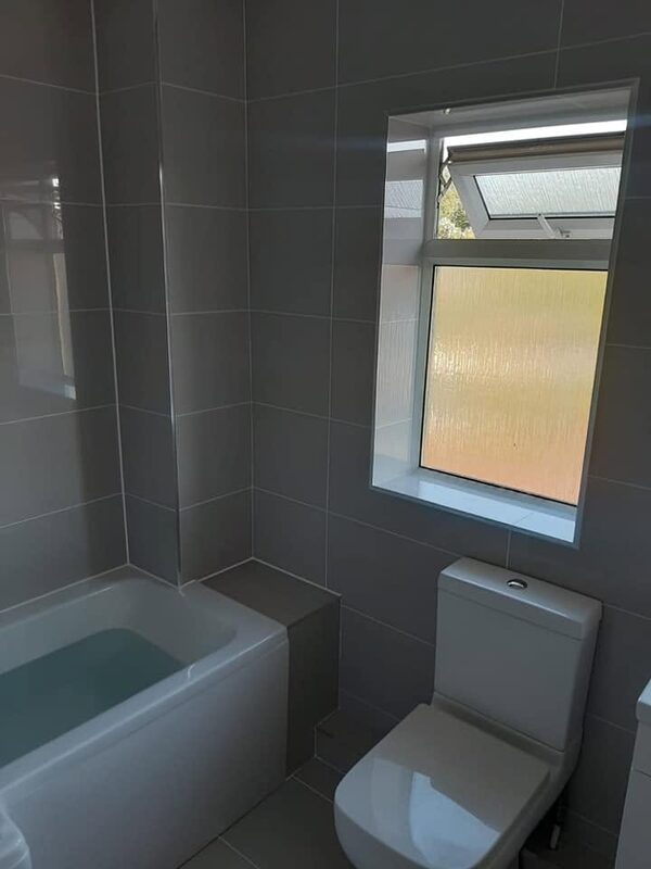 Corner of the same grey bathroom showing the bath, the toilet and the tiling running up to the window reveal