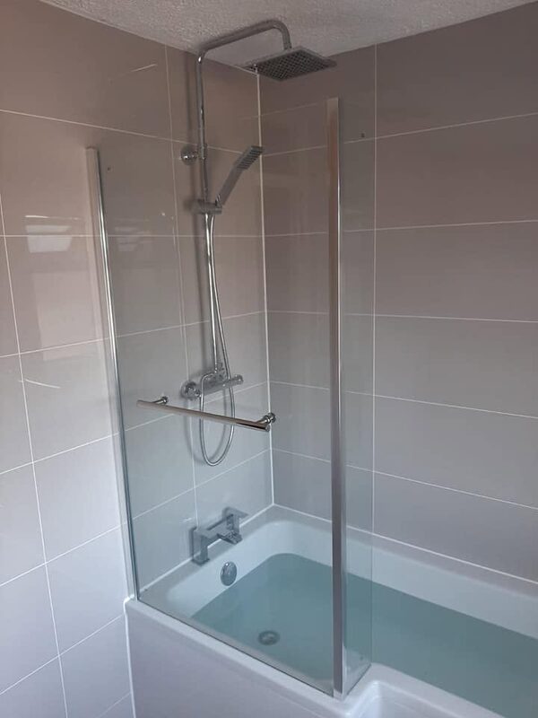 Round rainfall shower head and handset over a bath, with a chrome grab rail on grey tiles
