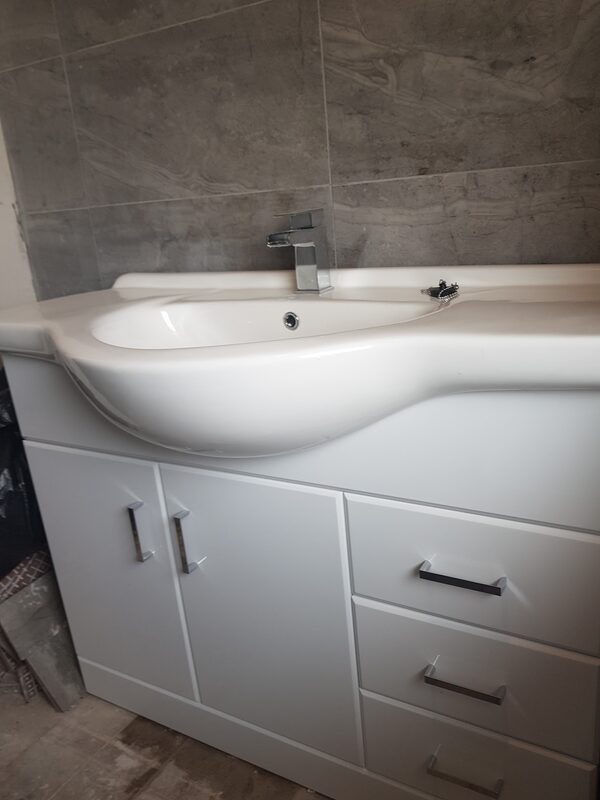 White vanity unit and basin against a grey tiled wall, photographed before the floor was laid
