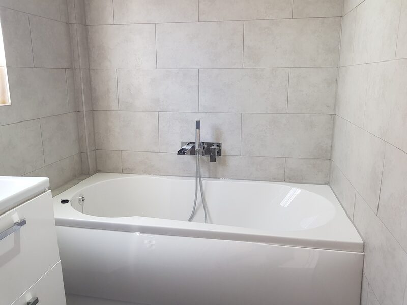 White bath with a light grey tiled surround and a wall-mounted mixer tap